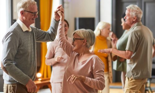 Group of smiling senior people dancing while enjoying activities in retirement home, copy space