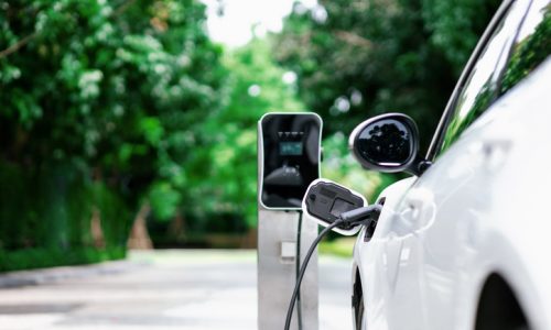 Focus closeup electric vehicle plugged in with EV charger device from blurred background of public charging station powered by renewable clean energy for progressive eco-friendly car concept.