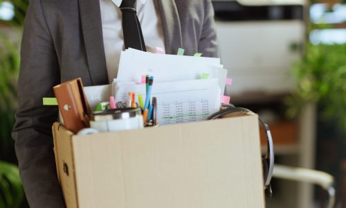 New job. Closeup on modern 40 years old woman employee in modern green office in grey business suit with personal belongings in cardboard box.
